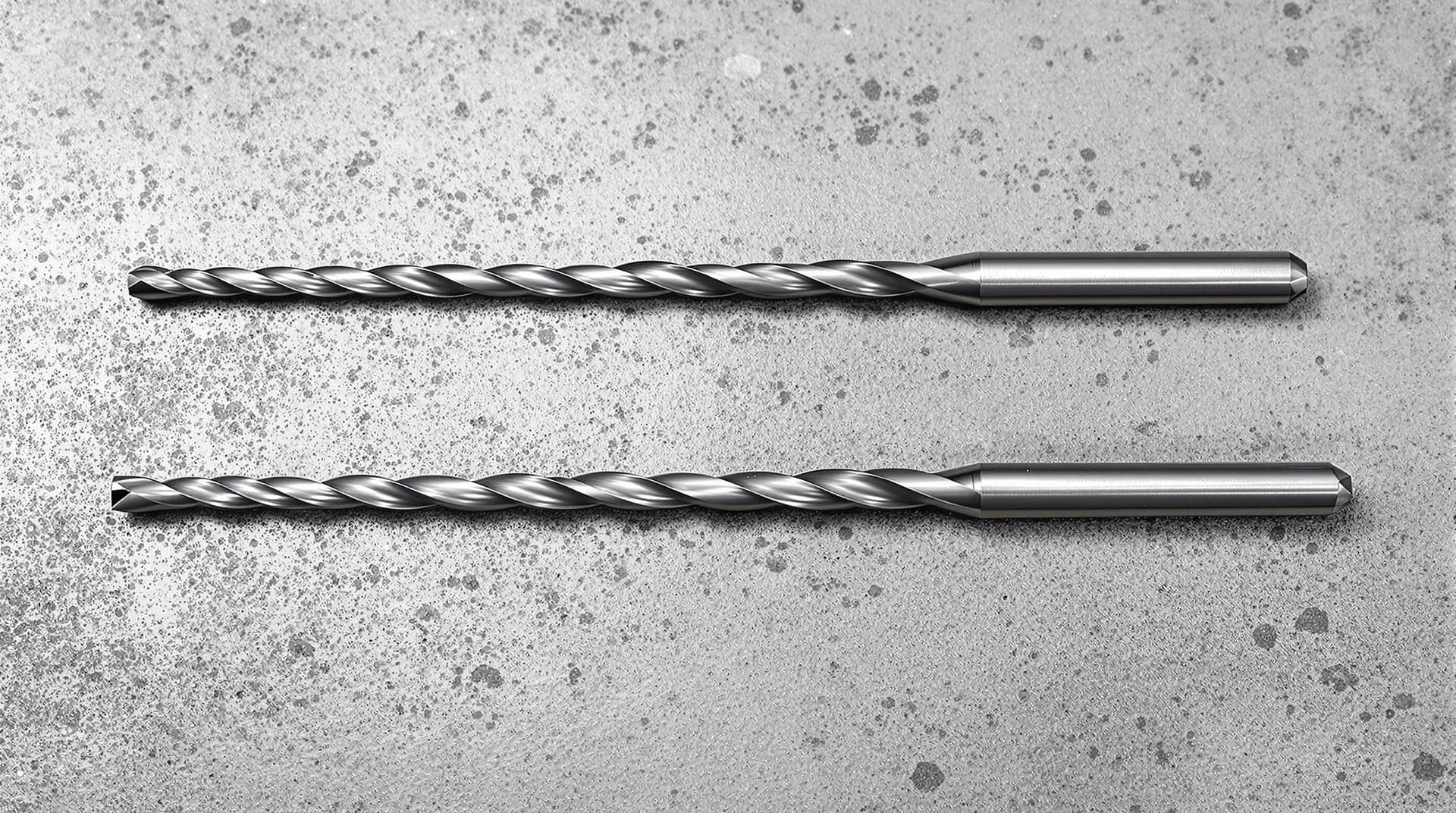 Two sets of drill bits laid out side by side for comparison, one set with carbide tips and one standard set, on a concrete surface