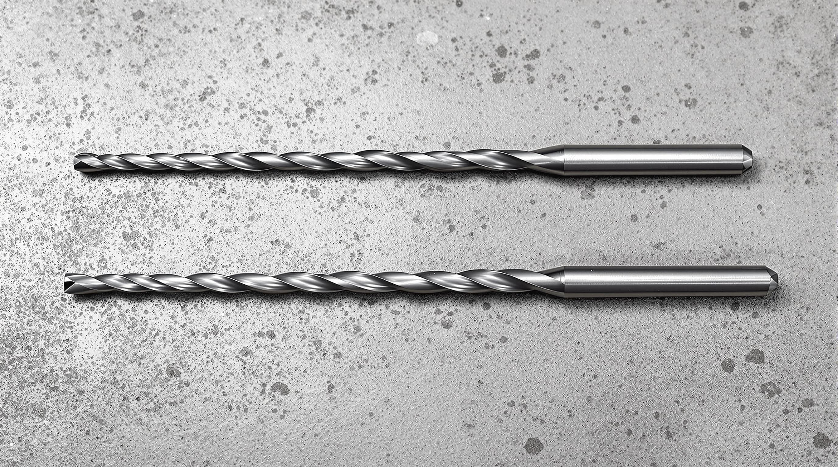 Two sets of drill bits laid out side by side for comparison, one set with carbide tips and one standard set, on a concrete surface